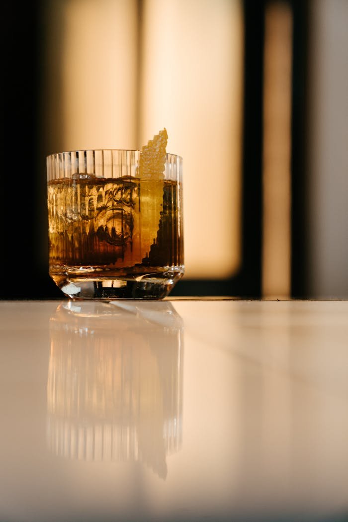A stylish cocktail with lemon zest garnish on a reflective bar counter, perfect for a classy evening.